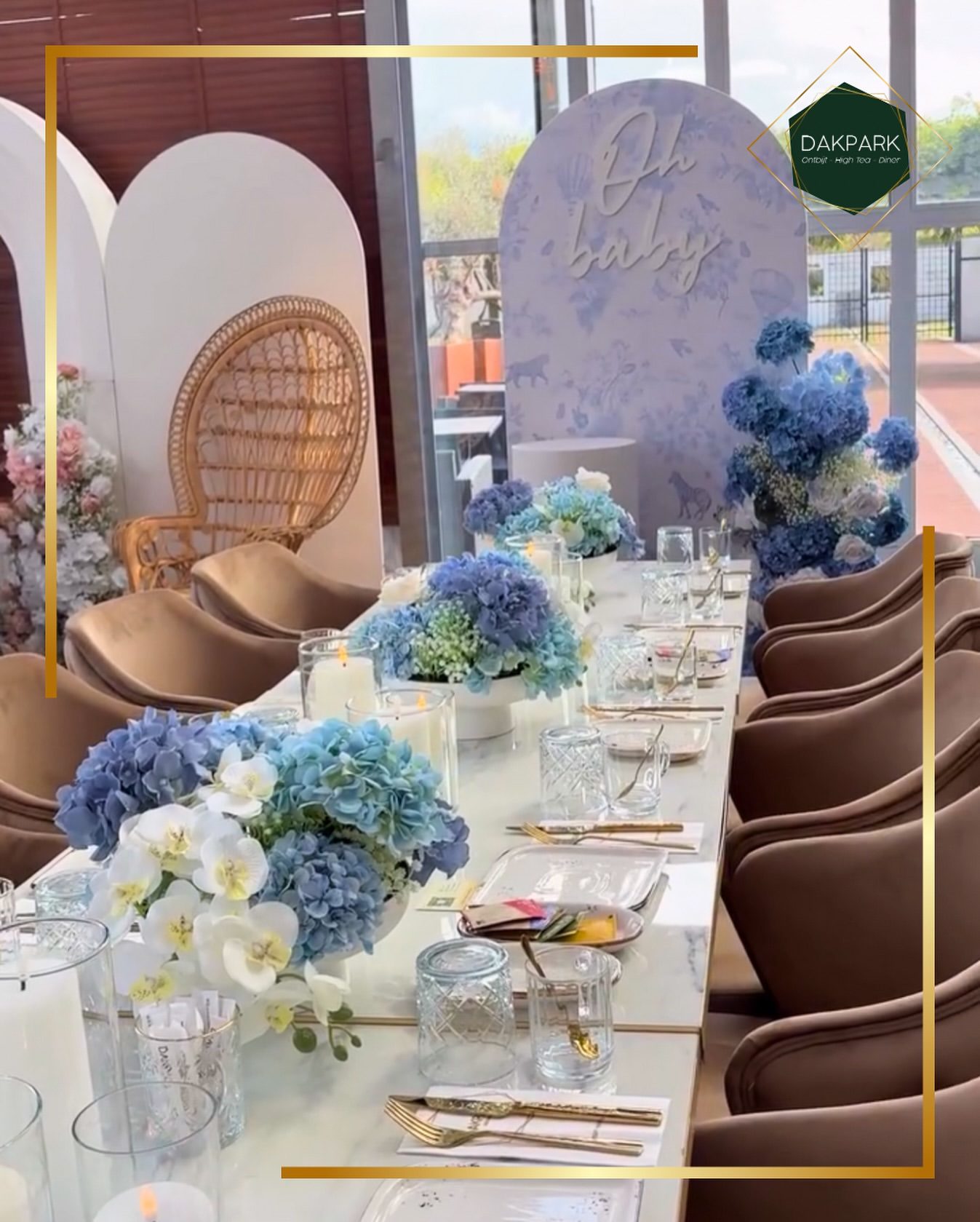 Babyshower-opstelling met 'Oh baby'-bord, blauwe hortensia's en rotan stoelen